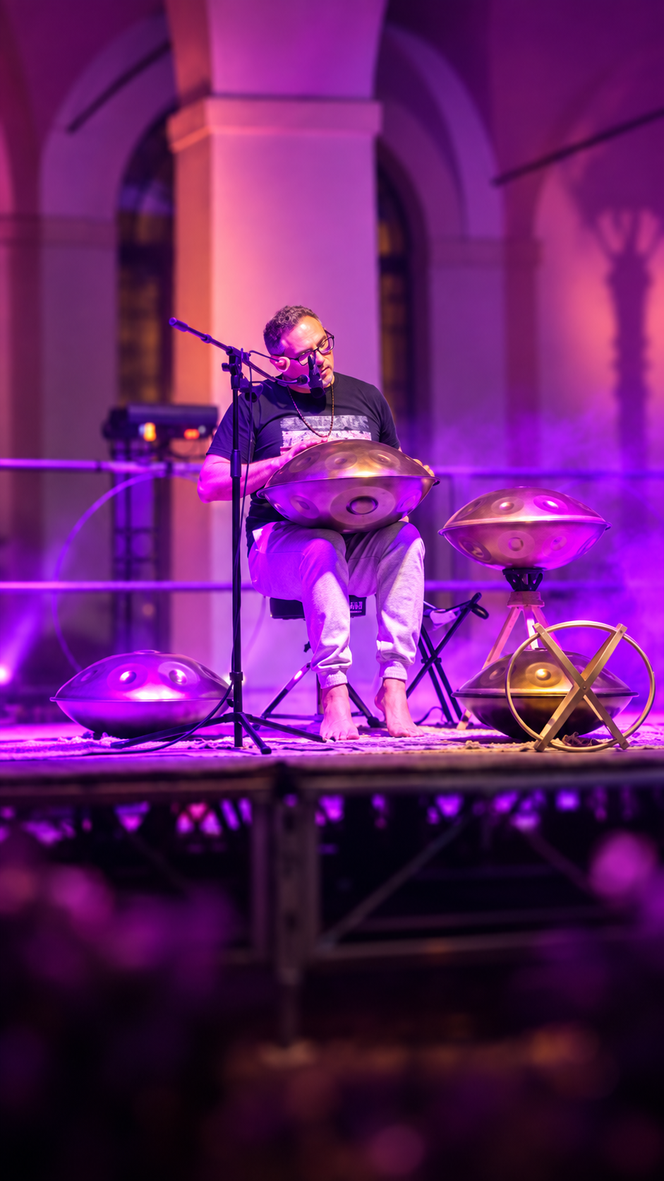 Musicista che suona un handpan dal vivo, circondato da altri handpan e luci viola sul palco